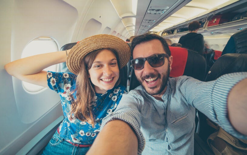 Young handsome couple taking a selfie on the airplane during flight around the world. They are a man and a woman, smiling and looking at camera. Travel, happiness and lifestyle concepts.