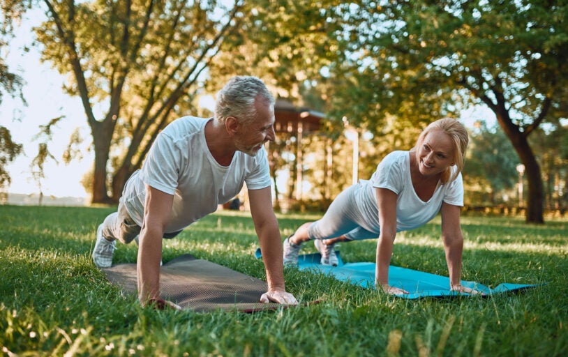 Senior couple is doing sport outdoors. Stretching in park during sunrise. Doing yoga together. Healthy lifestyle concept