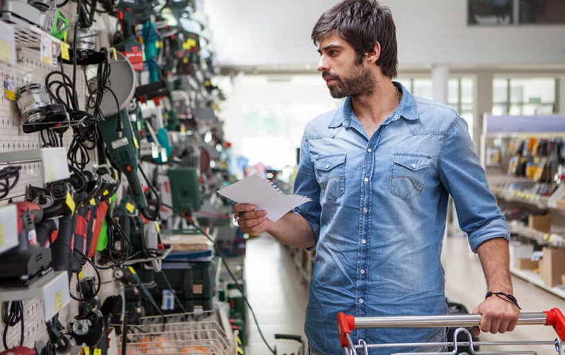 Man at a hardware store looking at power tools on a wall.