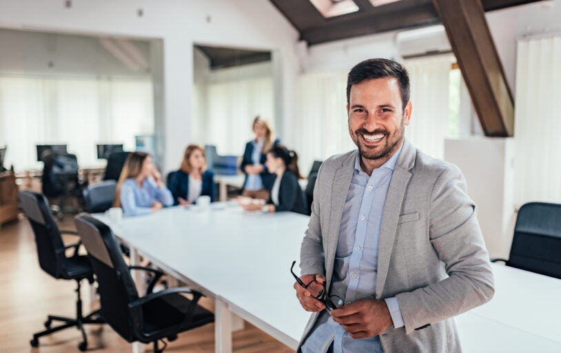 Man smiling at conference table in front of people