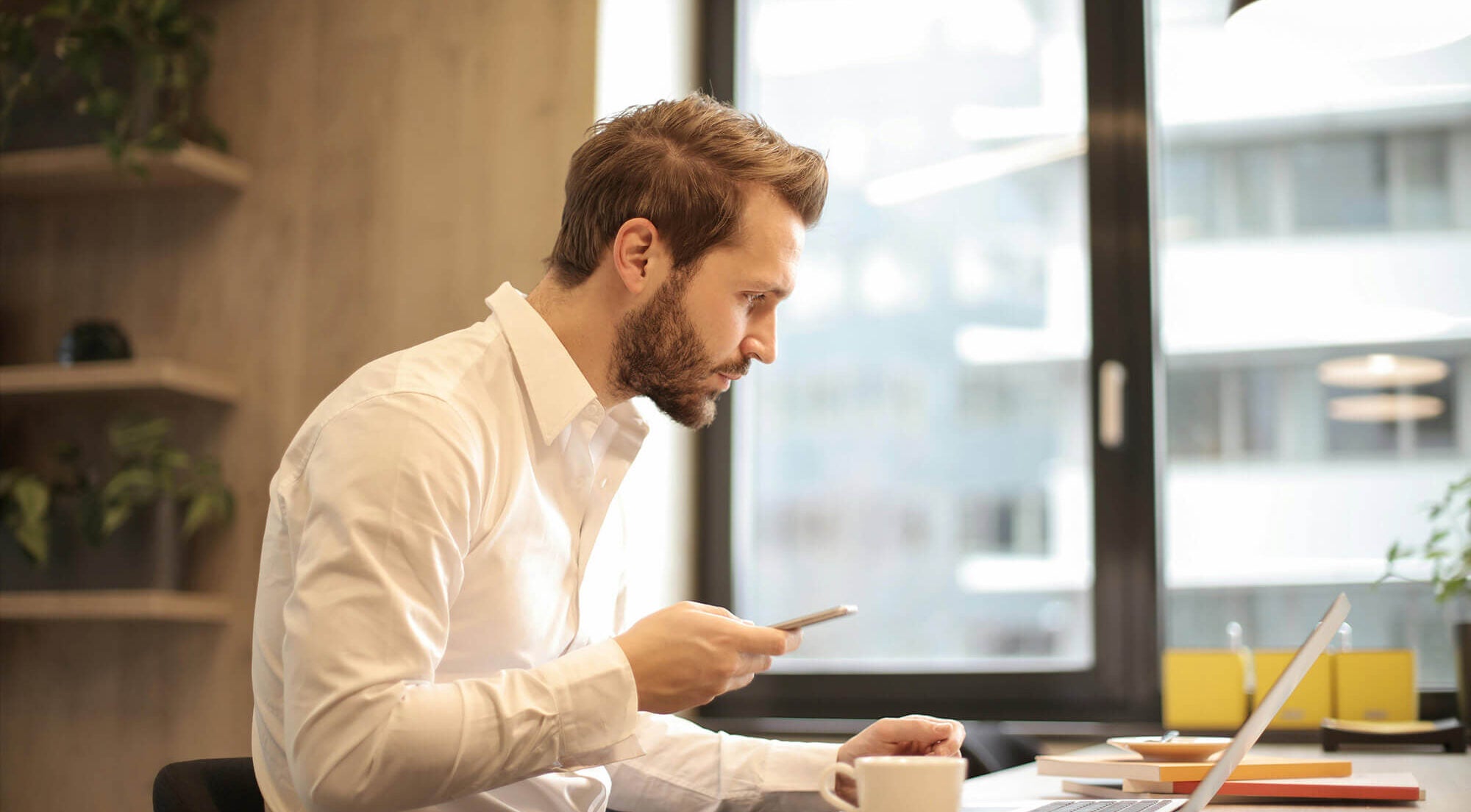 Man holding his phone looking at laptop