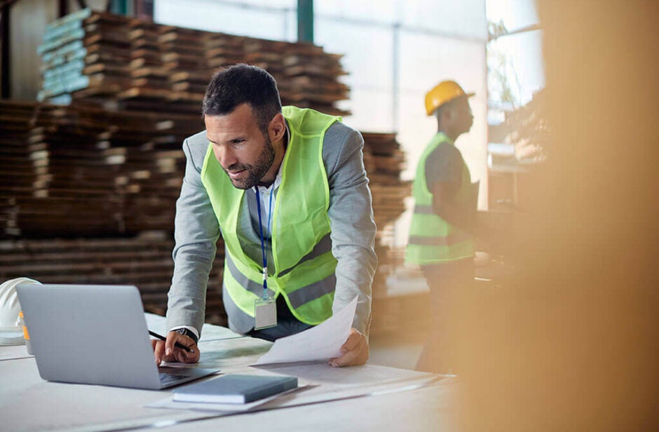 Man in a warehouse leaning over a laptop