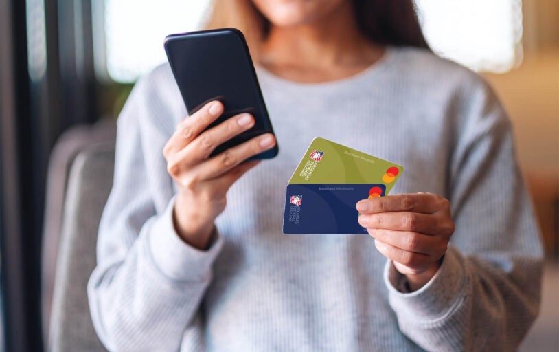 Woman holding a cell phone and two Arkansas Federal Credit Union business credit cards