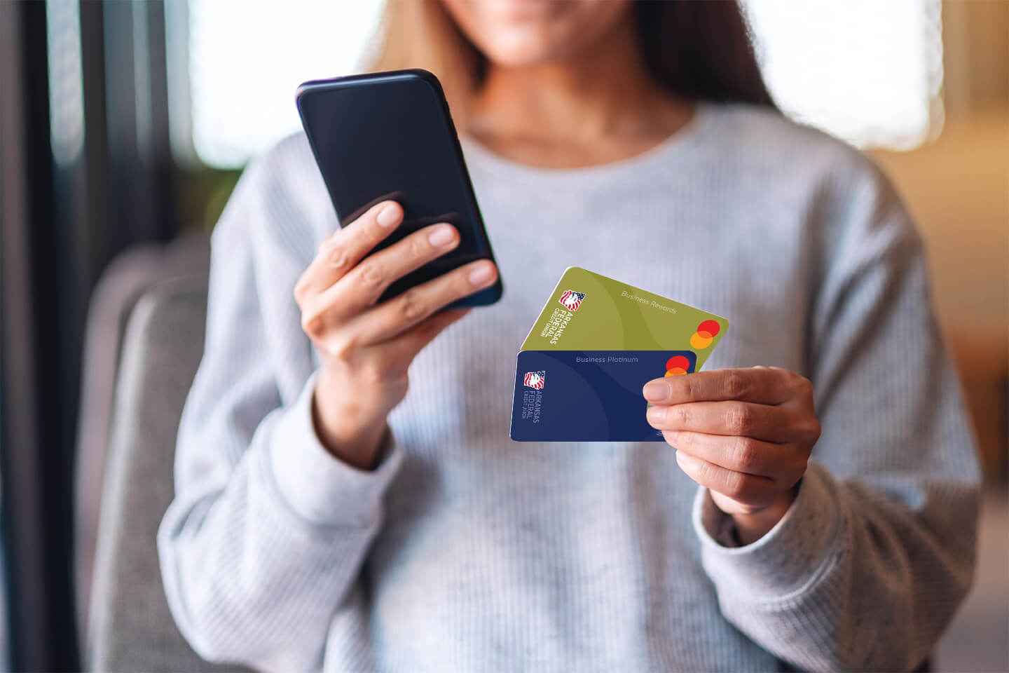 Woman holding a cell phone and two Arkansas Federal Credit Union business credit cards